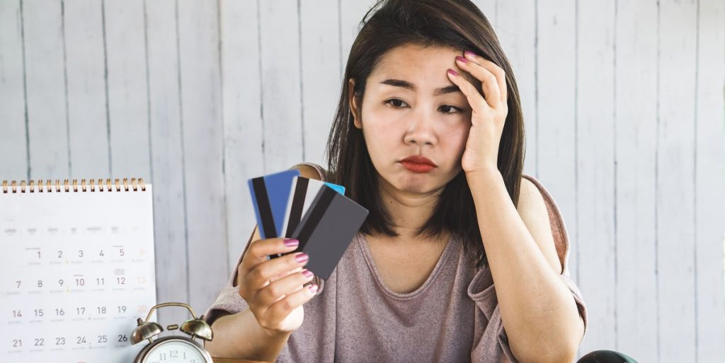 A foto mostra uma mulher aborrecida olhando para o cartão de crédito