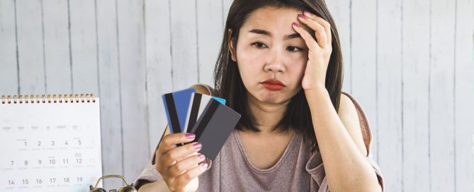A foto mostra uma mulher aborrecida olhando para o cartão de crédito