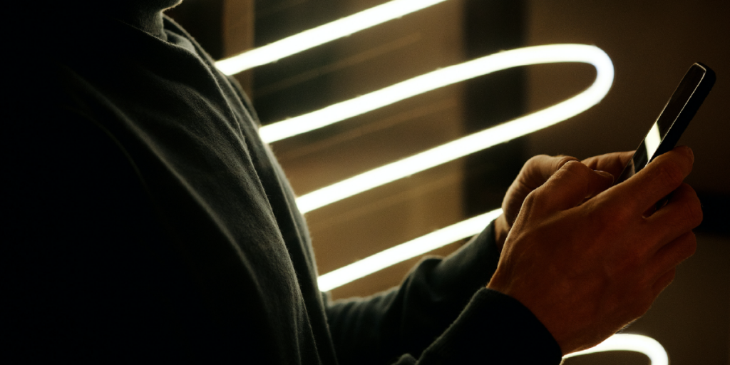 imagem escura de mãos segurando celular com luzes de led ao fundo