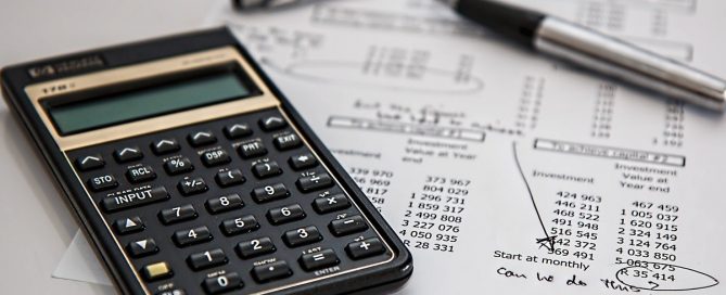 A imagem mostra uma calculadora e uma caneta em cima de papéis contendo contas financeiras.