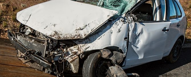 A imagem mostra um carro branco danificado por sofrer um acidente