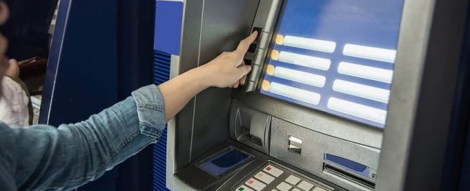 A imagem mostra a mão de uma mulher operando em um caixa eletrônico.