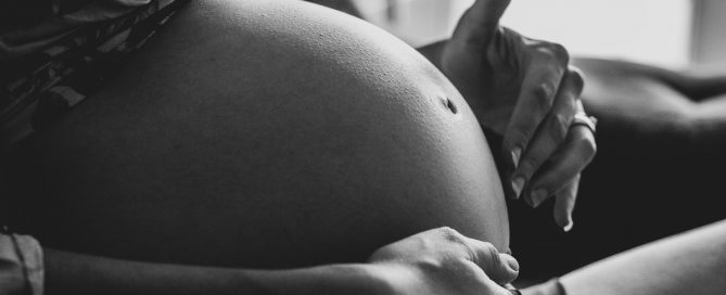 A imagem mostra a barriga de uma mulher grávida em preto e branco.