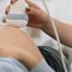 Médica fazendo ultrassom em barriga de mulher grávida.