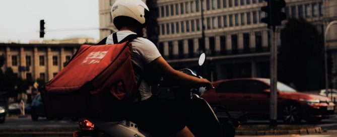 Um trabalhador dirigindo uma moto com uma mochila nas costas.