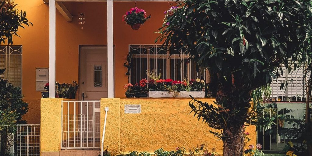 A imagem mostra a fachada de uma casa amarela com uma árvore na frente.