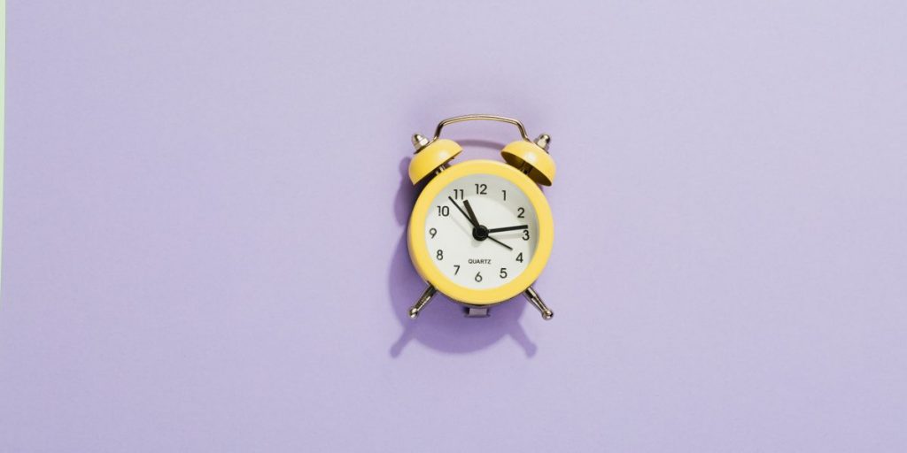 Um relógio despertador amarelo em um fundo lilás.