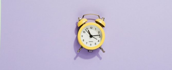 Um relógio despertador amarelo em um fundo lilás.