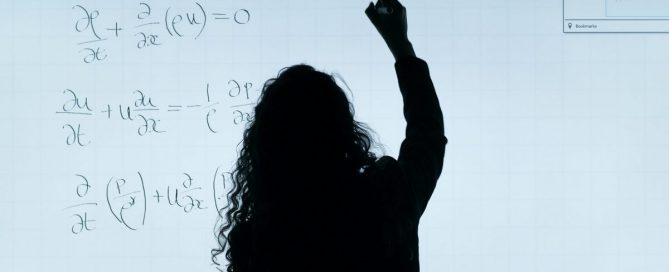 A silhueta de uma professora em frente a um quadro fazendo equações.
