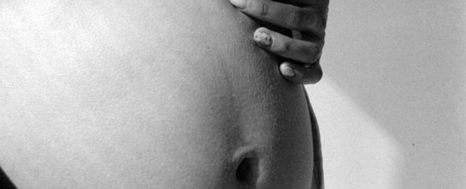 A barriga de uma mulher grávida em foto preto e branco.