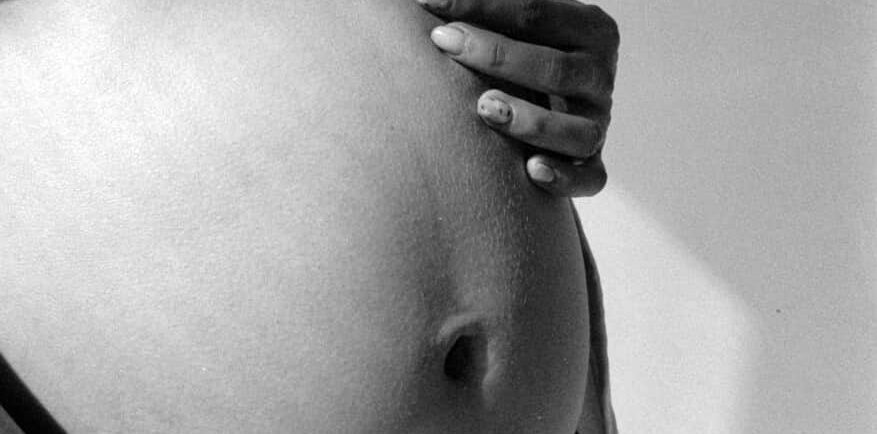 A barriga de uma mulher grávida em foto preto e branco.
