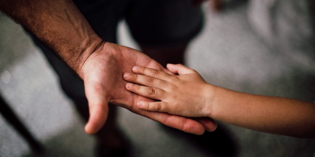 A mão de um adulto segurando a mão de uma criança.