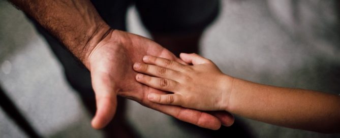 A mão de um adulto segurando a mão de uma criança.