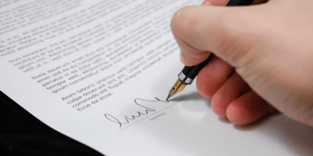 A mão de uma pessoa fazendo uma assinatura em um contrato.