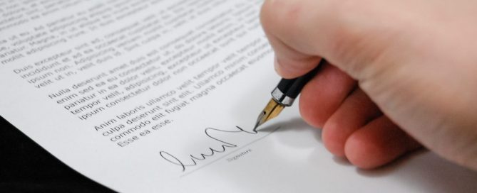 A mão de uma pessoa fazendo uma assinatura em um contrato.